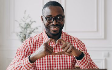 Happy african man gesturing heart symbol shape with hands during video call with family